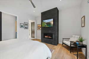 Bedroom with light wood-type flooring, a large fireplace, and ceiling fan