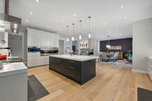 Kitchen with white cabinets, a large island, light hardwood / wood-style floors, and decorative light fixtures