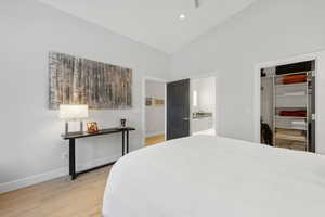 Bedroom featuring light wood-type flooring, high vaulted ceiling, ensuite bath, and a closet