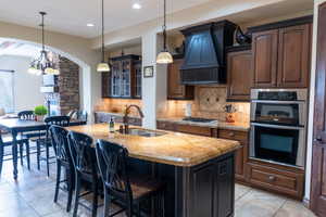 Kitchen with premium range hood, sink, an island with sink, dark brown cabinetry, and stainless steel appliances