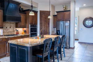 Kitchen featuring sink, pendant lighting, a center island with sink, custom range hood, and appliances with stainless steel finishes