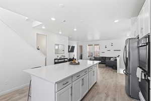 Kitchen with a breakfast bar, white cabinets, light hardwood / wood-style flooring, stainless steel fridge, and a kitchen island