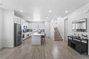 Kitchen featuring a center island, a kitchen breakfast bar, appliances with stainless steel finishes, light hardwood / wood-style floors, and white cabinetry