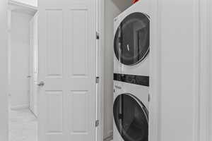 Washroom featuring stacked washer / dryer and light colored carpet