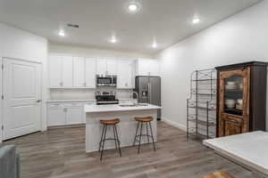 Kitchen featuring a center island with sink, sink, a kitchen bar, white cabinetry, and stainless steel appliances