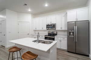 Kitchen featuring a breakfast bar, stainless steel appliances, a kitchen island with sink, sink, and white cabinetry