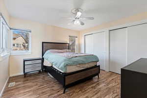 Bedroom with ceiling fan, dark hardwood / wood-style floors, and multiple closets