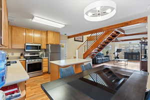 Kitchen with appliances with stainless steel finishes, sink, beamed ceiling, light hardwood / wood-style floors, and a kitchen island