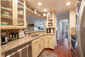 Kitchen featuring backsplash, dark wood-type flooring, sink, appliances with stainless steel finishes, and light stone counters