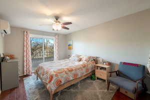 Bedroom with a wall mounted AC, access to outside, dark hardwood / wood-style floors, and ceiling fan