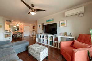 Living room with dark hardwood / wood-style flooring, a wall unit AC, and ornamental molding