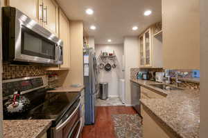 Kitchen featuring sink, light stone counters, dark hardwood / wood-style flooring, washer and clothes dryer, and appliances with stainless steel finishes