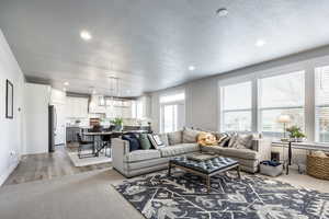 Living room with light hardwood / wood-style floors, a textured ceiling, a wealth of natural light, and a chandelier