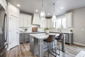 Kitchen with light wood-type flooring, custom exhaust hood, stainless steel appliances, a center island, and white cabinetry