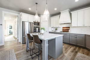 Kitchen with gray cabinetry, stainless steel appliances, light hardwood / wood-style floors, white cabinets, and custom range hood