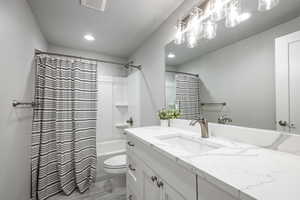 Full bathroom featuring shower / bathtub combination with curtain, vanity, a textured ceiling, and toilet