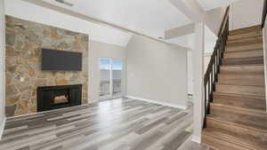 Unfurnished living room with hardwood / wood-style flooring, a stone fireplace, and lofted ceiling