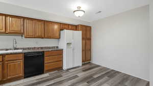 Kitchen with sink, black dishwasher, white refrigerator with ice dispenser, dark stone countertops, and light hardwood / wood-style floors