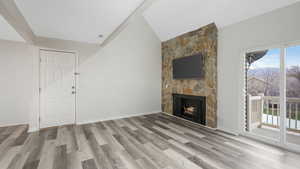 Unfurnished living room featuring a stone fireplace, light hardwood / wood-style floors, and lofted ceiling