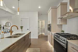 Kitchen featuring appliances with stainless steel finishes, light wood-type flooring, sink, wall chimney range hood, and hanging light fixtures