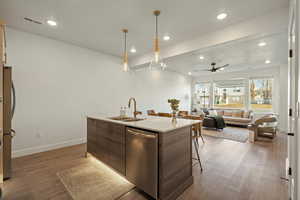 Kitchen with ceiling fan, sink, wood-type flooring, a center island with sink, and appliances with stainless steel finishes