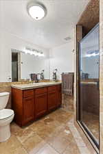 Bathroom with a textured ceiling, an enclosed shower, toilet, vanity, and tile walls