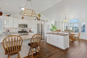 Kitchen featuring dark hardwood / wood-style flooring, stainless steel appliances, white cabinetry, and lofted ceiling