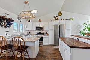 Kitchen with butcher block countertops, white cabinets, vaulted ceiling, and appliances with stainless steel finishes