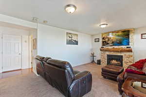 Living room with a stone fireplace, carpet floors, and a textured ceiling