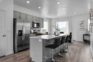 Kitchen featuring gray cabinetry, stainless steel appliances, a kitchen breakfast bar, a kitchen island with sink, and light wood-type flooring