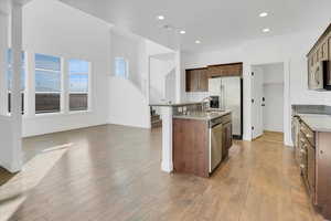 Kitchen featuring granite countertops, a center island with sink, stainless steel appliances, and light wood-type flooring