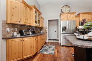 Kitchen featuring lofted ceiling, dark hardwood / wood-style flooring, stainless steel fridge with ice dispenser, and tasteful backsplash