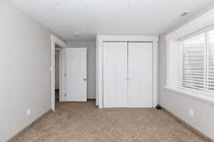 Unfurnished bedroom featuring light carpet, a closet, and a textured ceiling