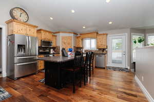 Kitchen with a kitchen bar, backsplash, stainless steel appliances, dark wood-type flooring, and a kitchen island