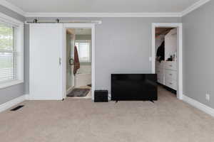 Bedroom featuring a barn door, light carpet, and ornamental molding