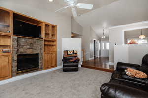 Carpeted living room with a fireplace, ceiling fan, and lofted ceiling