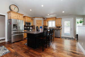 Kitchen with dark wood-type flooring, a kitchen breakfast bar, backsplash, a kitchen island, and appliances with stainless steel finishes