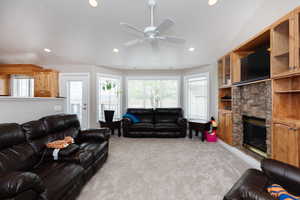 Carpeted living room with vaulted ceiling, a stone fireplace, and ceiling fan