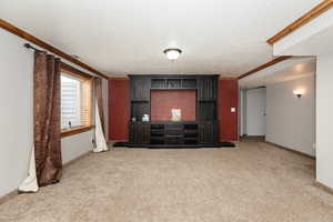 Unfurnished living room featuring carpet floors, a textured ceiling, and ornamental molding