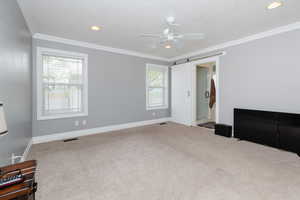 Carpeted bedroom featuring a barn door, multiple windows, crown molding, and ceiling fan