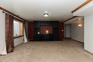 Unfurnished living room featuring carpet, ornamental molding, and a textured ceiling