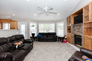 Living room featuring light colored carpet, ceiling fan, a stone fireplace, and lofted ceiling