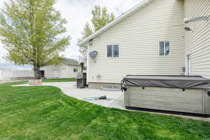 Back of house with a hot tub, a patio area, and a lawn