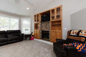 Living room featuring a fireplace, light carpet, ceiling fan, and lofted ceiling