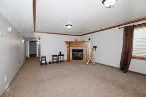 Living room with carpet flooring, crown molding, a fireplace, and a textured ceiling