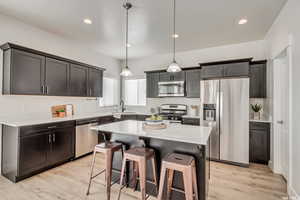 Kitchen with a center island, sink, light hardwood / wood-style flooring, appliances with stainless steel finishes, and decorative light fixtures