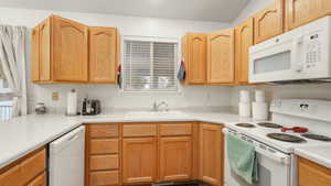 Kitchen with white appliances, lofted ceiling, and sink