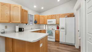 Kitchen featuring lofted ceiling, white appliances, sink, light hardwood / wood-style floors, and kitchen peninsula