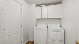 Clothes washing area with hardwood / wood-style flooring, cabinets, and washing machine and clothes dryer