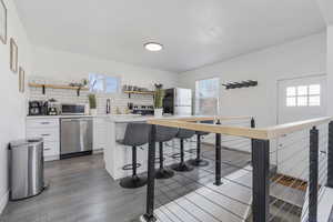 Kitchen featuring white cabinetry, sink, stainless steel appliances, dark LVP wood-style floors, and a four-seater island